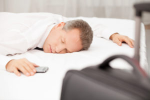 Tired and overworked. Tired grey hair man in shirt and tie sleeping on bed while luggage laying on foreground